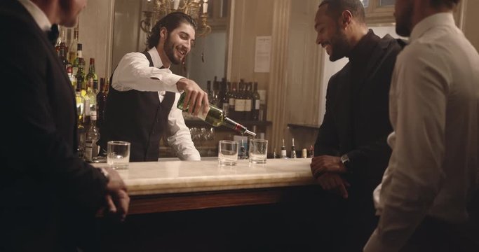 Male bartender serving drinks to group of men at party. Barman serving alcohol to guest at a nightclub. 
