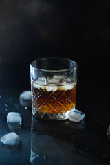 Glass of whiskey or bourbon with ice on black stone table. Glass of whiskey with ice and a square decanter. Glass of scotch whiskey