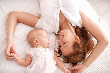 Loving mother and baby lying on bed. They enjoy spending time together.