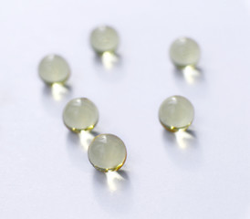Transparent round capsules of vitamins - Fish oil pills close-up. Small gold-yellow balls on a white background. Concept of treatment and prevention of health. 