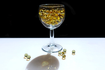Fish oil pills in a glass. Transparent round capsules of vitamin on a black and white background. Small gold-yellow balls close-up, side view. Concept of treatment and prevention of health. 