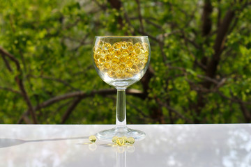 Fish oil pills in a wine glass. Transparent round capsules of vitamin on a nature background. Small gold-yellow balls close-up. Concept of treatment and prevention of health. 