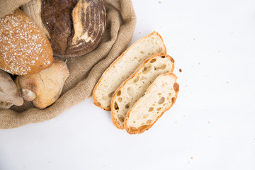 Sliced bread and freshly baked buns in rustic burlap sack and wheat ears. Closeup shot, top view, copy space. Isolated object on white background. Baking or homemade bread concept