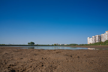 border of a large multi-story city and countryside. tall houses on the banks of a shallow river. the concept of urban expansion and the destruction of small rural settlements