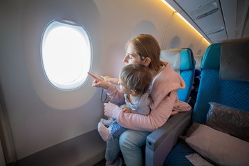 young beautiful mother sits in an airplane chair holds on her lap a little cute baby and points...