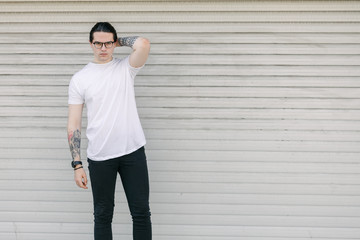 Hipster handsome male model wearing white blank t-shirt with space for your logo or design in casual urban style. He is holding a skateboard