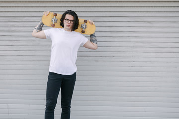 Hipster handsome male model wearing white blank t-shirt with space for your logo or design in casual urban style. He is holding a skateboard © 4Max