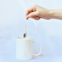 Hand holds tea bag over a mug