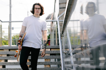 Hipster handsome male model wearing white blank t-shirt with space for your logo or design in casual urban style. He is holding a skateboard © 4Max