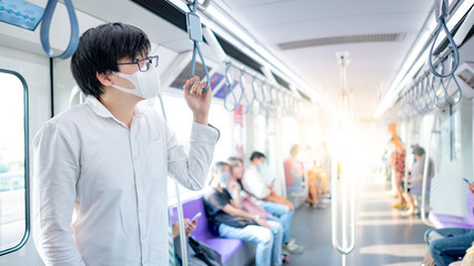 Asian man wearing surgical face mask holding handrail on skytrain or urban train. Coronavirus (COVID-19) outbreak prevention in public transportation. Health awareness for pandemic protection