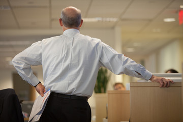 Rear view of businessman holding documents with and on hip while standing at office