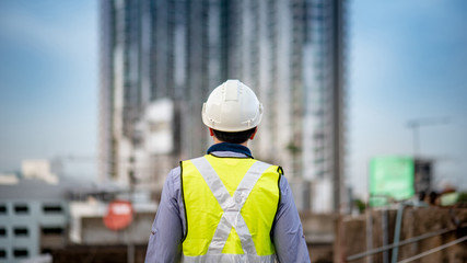 Asian maintenance worker man with safety helmet and green vest standing at construction site. Civil engineering, Architecture builder and building service concepts