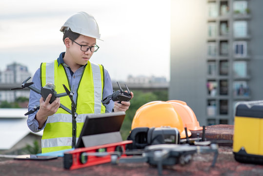 Asian engineer man working with drone, laptop and working tools at construction site. Male worker using unmanned aerial vehicle (UAV) for land and building site survey in civil engineering project.