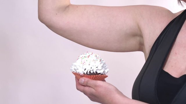 A middle-aged woman, showing saggy skin on her hand, holding a cupcake with the other hand, on a white background.