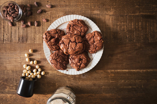 Homemade dark chocolate cookies with macadamia nuts cocoa beans and sugar on a rustic wooden table