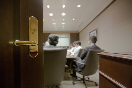Businessmen in meeting as seen through open door.