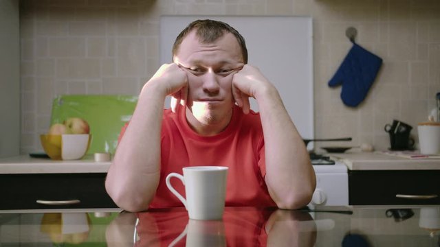 Tired emotionless man with an empty look looks directly supporting his head with his hands