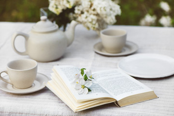 Open book with flowers, tea cups, tea pot and branch of lilac.