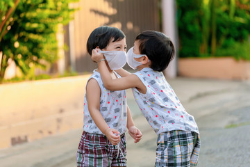 Kid in safety wearing mask in town. Twin Children wearing medical face mask outdoor. Twin Child  helps to put a mask on his face to his brother. Protect himself from pollution or pm 2.5
