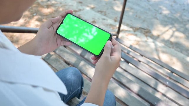 A female mobile phone with a green screen Women use mobile phones while walking in the park Rear view image A woman phone with a green horizontal screen
