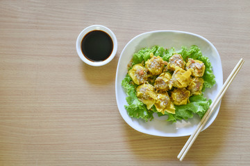 Dumpling arranged on a plate with a sauce for dunking on a wooden table.
Shu Mai served on a plate on a wooden background.