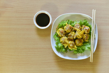 Dumpling arranged on a plate with a sauce for dunking on a wooden table.
Shu Mai served on a plate on a wooden background.