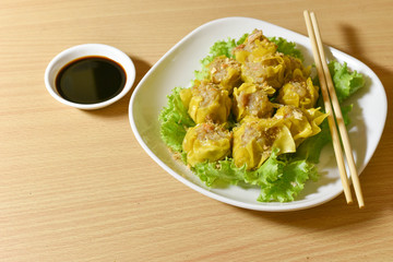 Dumpling arranged on a plate with a sauce for dunking on a wooden table.
Shu Mai served on a plate on a wooden background.