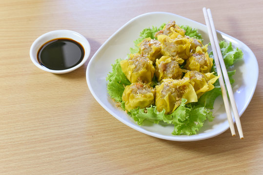 Dumpling arranged on a plate with a sauce for dunking on a wooden table.
Shu Mai served on a plate on a wooden background.