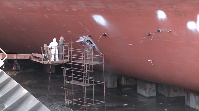 worker painting ship in shipyard drydock