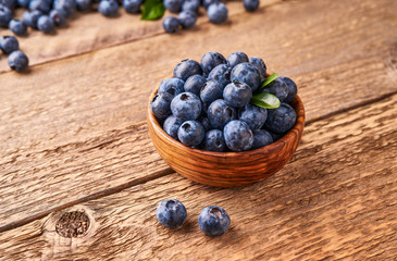 Fresh blueberries with blueberry leaves in wooden bowl on wooden background.