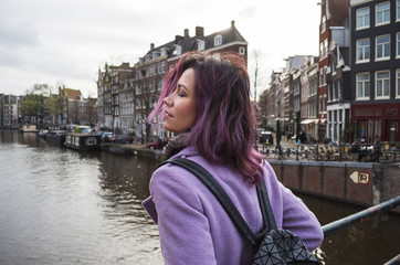 Fototapeta na wymiar Girl in the coat and backpack enjoying city. Young woman looking to the side on Amsterdam channel, Netherlands