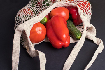 Eco bag string bag with vegetables cucumbers and tomatoes on a black background. Zero West