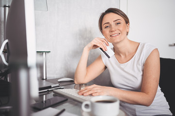 Beautiful happy woman holding credit card in hand and using laptop computer keyboard. Businesswoman or entrepreneur working. Online shopping, e-commerce, internet banking, spending money concept