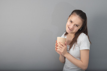 A boost of energy in a glass of invigorating coffee. Young woman drinks hot drink on gray background