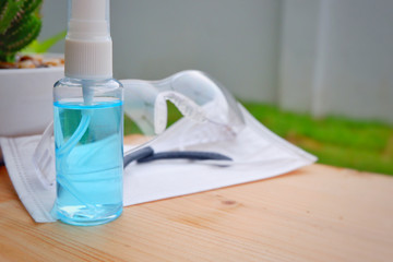 Alcohol gel bottle,eye glasses and Hygienic mask(Face mask) on wood.Alcohol and a white surface cleaning cloth on wood shelf for cleaning our hand before to take anything.Close up.
