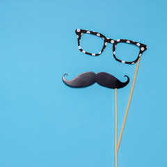 Photo booth props moustache and glasses on blue background. Greeting card for father's day or men's health awareness month campaign concept. Flat lay, space for text