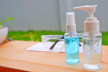 Alcohol gel bottle,eye glasses and Hygienic mask(Face mask) on wood.Alcohol and a white surface cleaning cloth on wood shelf for cleaning our hand before to take anything.Close up.
