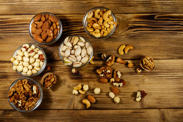 Assortment of nuts on wooden table. Almond, hazelnut, pistachio, walnut and cashew in glass bowls. Top view. Healthy eating concept