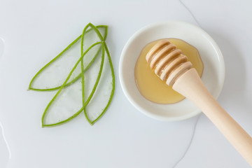 aloe vera leaves chopped into thin slices, bowl with honey and honey-pot grinder with white background