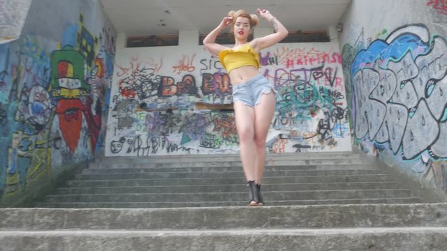 The girl is dancing kizomba. Sexy funny woman dancing african dance on graffiti background. Beautiful young dancer seductively dances and moves her buttocks. Graffiti, skate park.