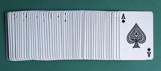 A deck of playing cards laid out on a green table. Top card ace of spades.