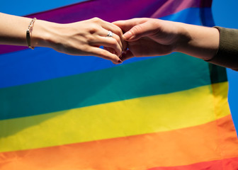 hands of a lesbian couple outdoors. LGBT rainbow flag.