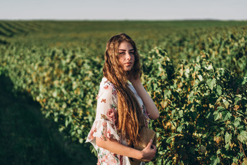 beautiful woman with long curly hair and freckles face on currant field background. Girl in a light dress walks in the summer sunny day