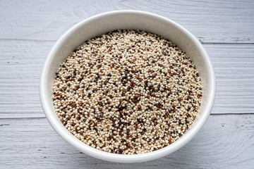 Mixed raw quinoa in bowl on white wooden kitchen table. top view. Healthy and diet super food product. vegan food