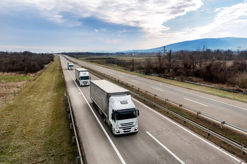 Convoy of Three White transportation  trucks in line as a caravan or convoy on a country highway under a blue sky