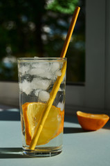 lemon water with ice in a glass glass with a yellow tube on the window lies half a lemon