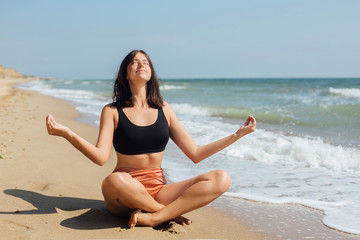 Fototapeta na wymiar Yoga and meditation on beach. Young beautiful woman practicing yoga, sitting on seashore and meditaning. Mental health and self care concept. Summer vacation