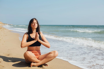 Fototapeta na wymiar Mental health and self care concept. Young beautiful woman practicing yoga on the beach, sitting on sand and meditaning. Happy girl relaxing on seashore on summer vacation
