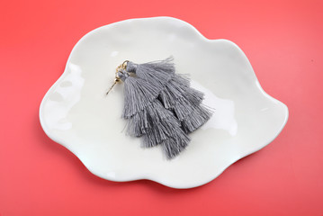 Gray tassel earrings on a white plate with a red background