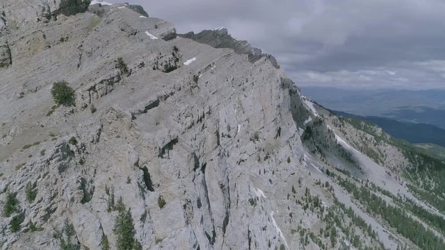 AERIAL DRON ORBIT DISCOVERING STUNNING HUGE MOUNTAIN RANGE IN SPRING WITH SNOW AND GREEN FIR TREES